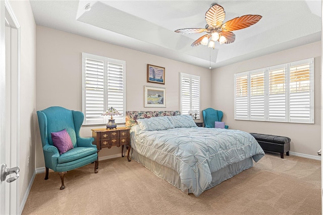 bedroom featuring ceiling fan, a tray ceiling, and light carpet