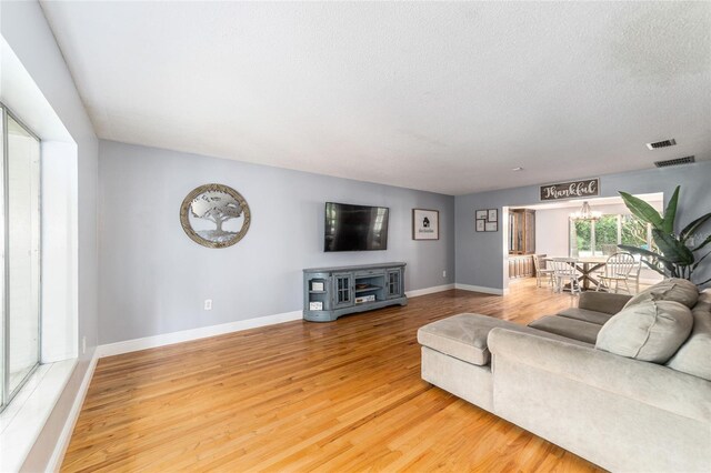 living area featuring baseboards, visible vents, a textured ceiling, and light wood finished floors