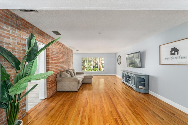 unfurnished living room featuring a textured ceiling, brick wall, light hardwood / wood-style floors, and a wood stove