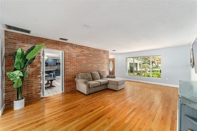 unfurnished living room featuring light wood-style floors, visible vents, a textured ceiling, and brick wall