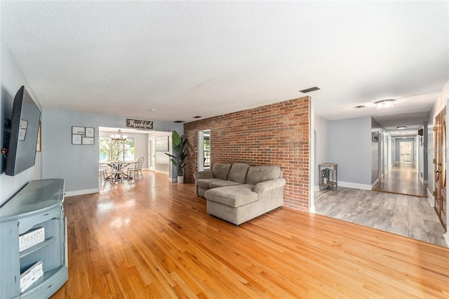 unfurnished living room featuring light hardwood / wood-style flooring, a textured ceiling, and brick wall