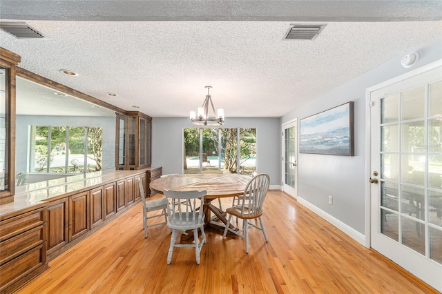 dining space featuring light wood-type flooring, a notable chandelier, and a textured ceiling