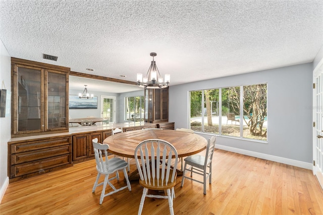 dining area with a textured ceiling, light hardwood / wood-style floors, and a chandelier