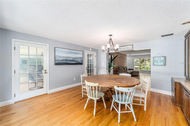 dining space featuring a textured ceiling, a notable chandelier, visible vents, baseboards, and light wood finished floors