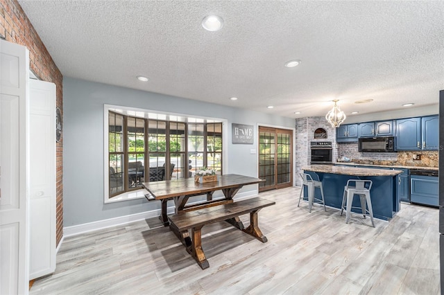 dining space with light hardwood / wood-style floors, an inviting chandelier, a textured ceiling, and a brick fireplace