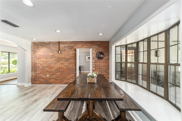 dining room featuring a textured ceiling, brick wall, and hardwood / wood-style floors