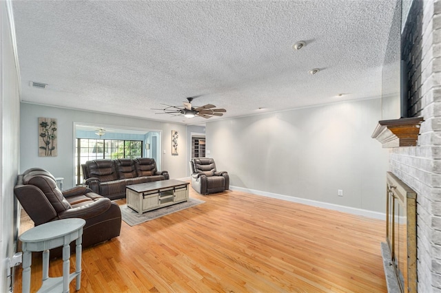 living room featuring ceiling fan, a brick fireplace, light hardwood / wood-style floors, a textured ceiling, and crown molding