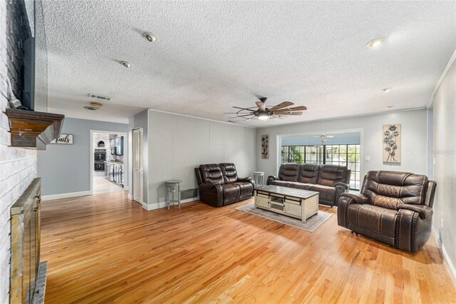 living room with a fireplace, ceiling fan, a textured ceiling, and light wood-type flooring