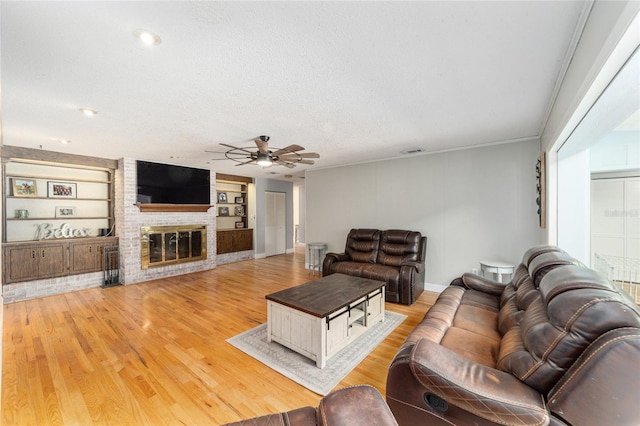 living room featuring visible vents, a ceiling fan, light wood-style flooring, a textured ceiling, and a brick fireplace