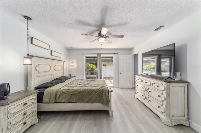 bedroom featuring light wood-type flooring, a ceiling fan, visible vents, and a textured ceiling