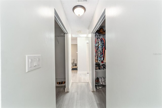 hallway with light wood-type flooring and a textured ceiling