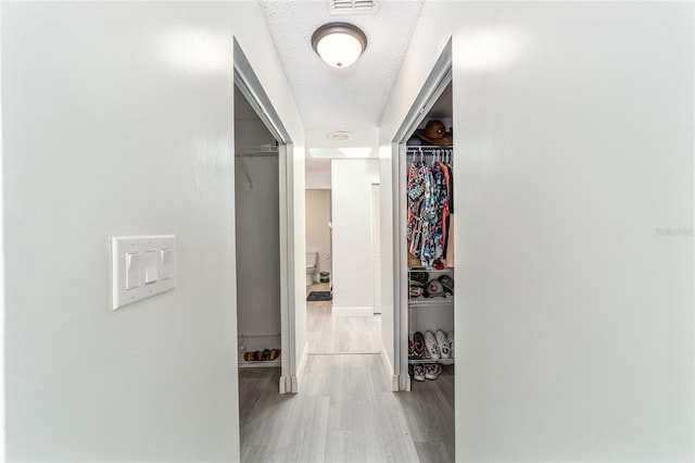 hall with visible vents, a textured ceiling, and wood finished floors