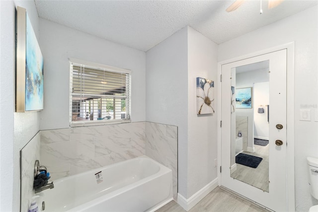 bathroom featuring hardwood / wood-style floors, a tub to relax in, a textured ceiling, ceiling fan, and toilet