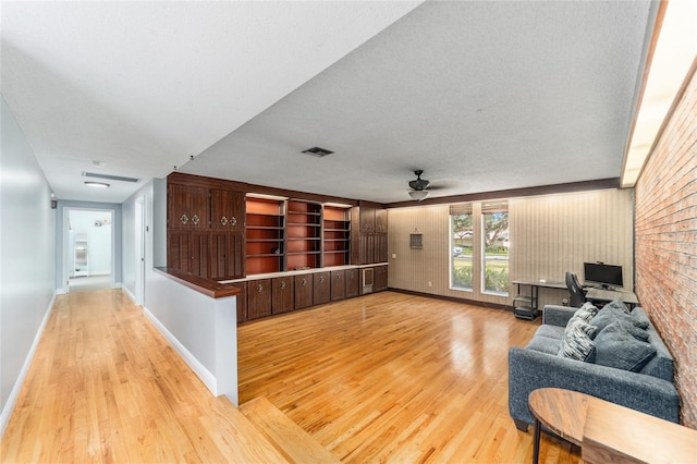 living room featuring visible vents, baseboards, a ceiling fan, light wood-style flooring, and a textured ceiling