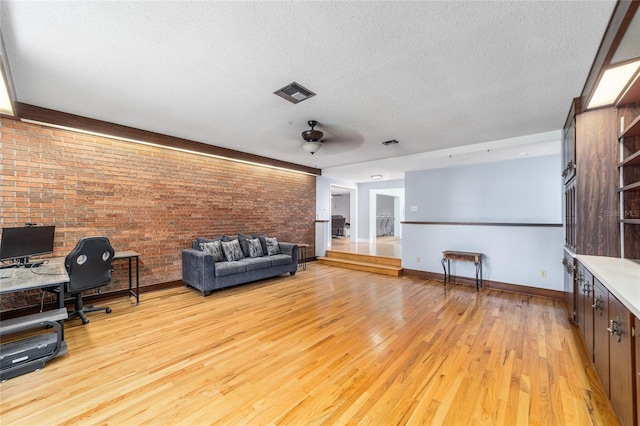 unfurnished living room featuring ceiling fan, a textured ceiling, light hardwood / wood-style floors, and brick wall