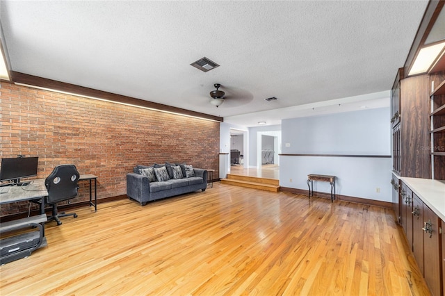 interior space with visible vents, light wood-style flooring, ceiling fan, a textured ceiling, and brick wall