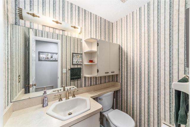 bathroom with toilet, wallpapered walls, and vanity