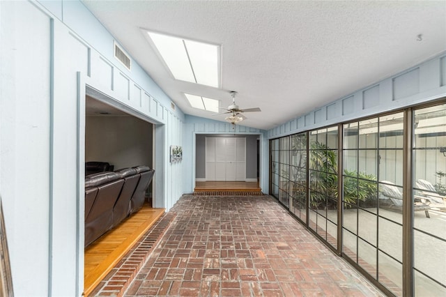 unfurnished sunroom featuring vaulted ceiling with skylight, visible vents, and a ceiling fan