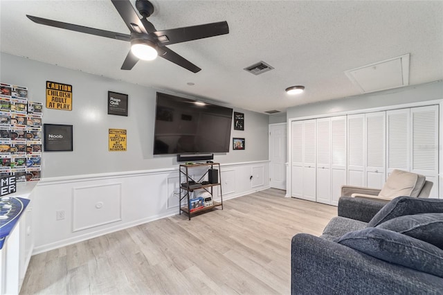 living area with a textured ceiling, ceiling fan, a wainscoted wall, wood finished floors, and visible vents