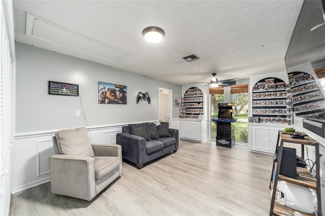 living room featuring light hardwood / wood-style floors, ceiling fan, and a textured ceiling