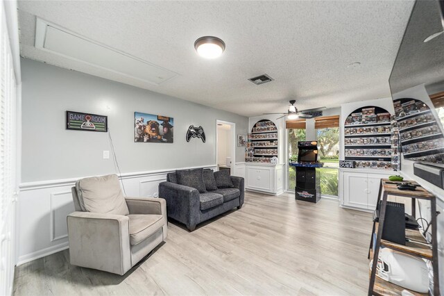 living room featuring visible vents, attic access, light wood-style floors, wainscoting, and a textured ceiling