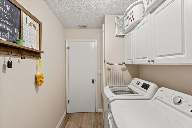 laundry area featuring washer and dryer, cabinets, light hardwood / wood-style floors, and a textured ceiling