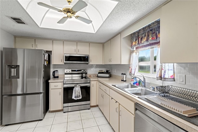 kitchen featuring stainless steel appliances, a textured ceiling, cream cabinetry, and sink