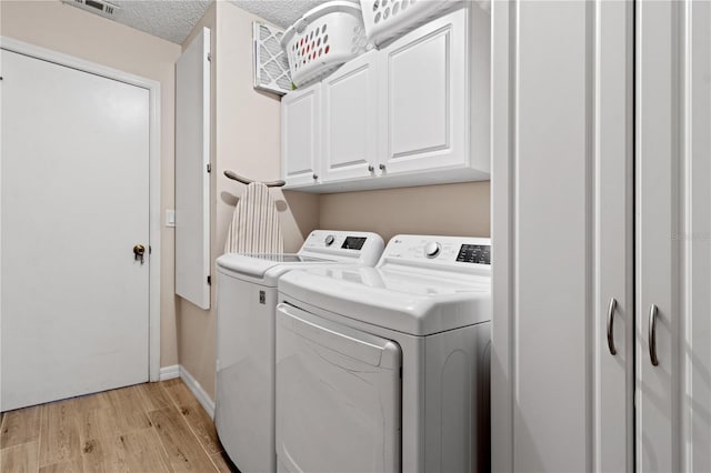 clothes washing area with cabinets, a textured ceiling, light hardwood / wood-style flooring, and independent washer and dryer