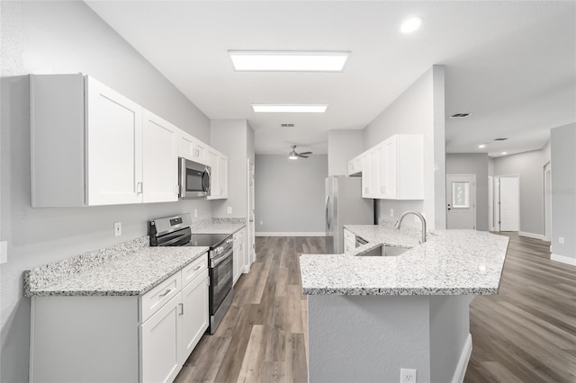 kitchen with sink, appliances with stainless steel finishes, white cabinetry, light stone counters, and kitchen peninsula