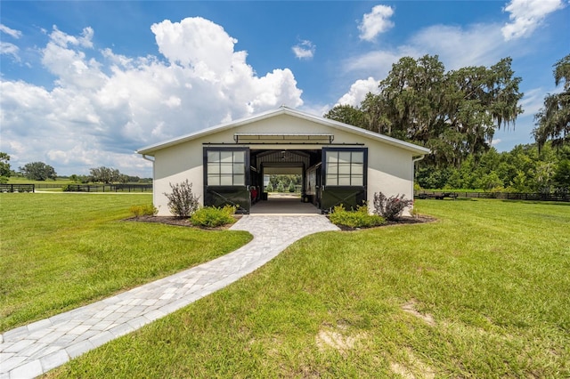 entrance to property featuring a rural view, a lawn, fence, and stucco siding