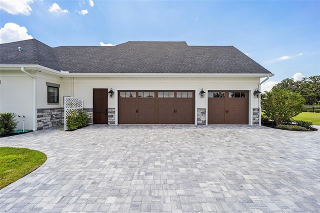 exterior space featuring decorative driveway, stone siding, a shingled roof, and stucco siding