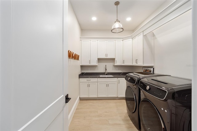 clothes washing area with light hardwood / wood-style floors, cabinets, sink, and washing machine and clothes dryer