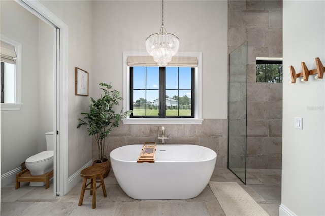 bathroom with shower with separate bathtub, an inviting chandelier, toilet, and tile walls