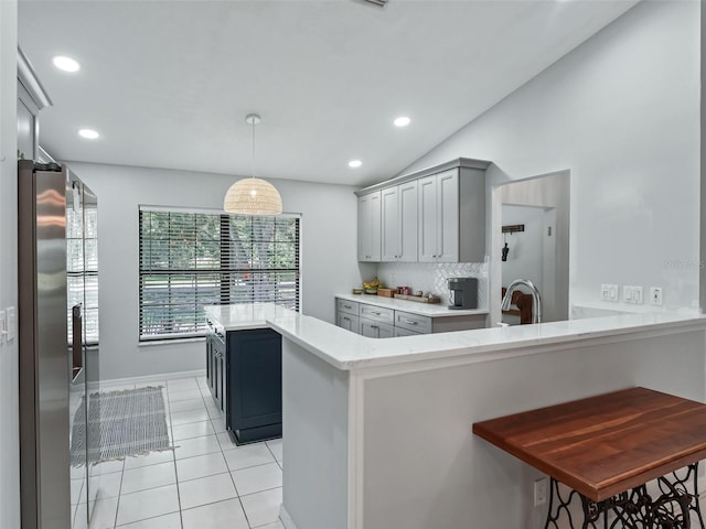 kitchen featuring kitchen peninsula, decorative backsplash, a kitchen bar, gray cabinetry, and hanging light fixtures