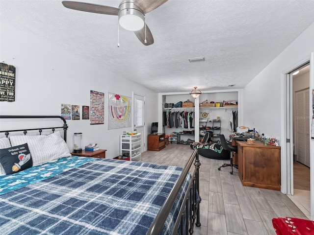 bedroom featuring a ceiling fan, wood finish floors, visible vents, and a textured ceiling