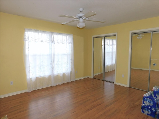 unfurnished bedroom with multiple closets, hardwood / wood-style floors, and ceiling fan