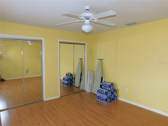 unfurnished bedroom with two closets, ceiling fan, and hardwood / wood-style flooring