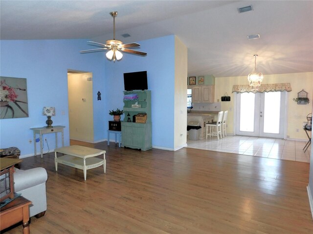 living room with lofted ceiling, tile patterned floors, ceiling fan with notable chandelier, and french doors