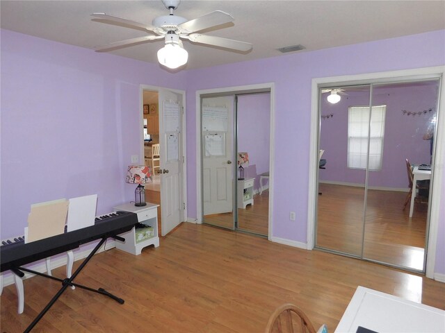 bedroom with two closets, light hardwood / wood-style flooring, and ceiling fan