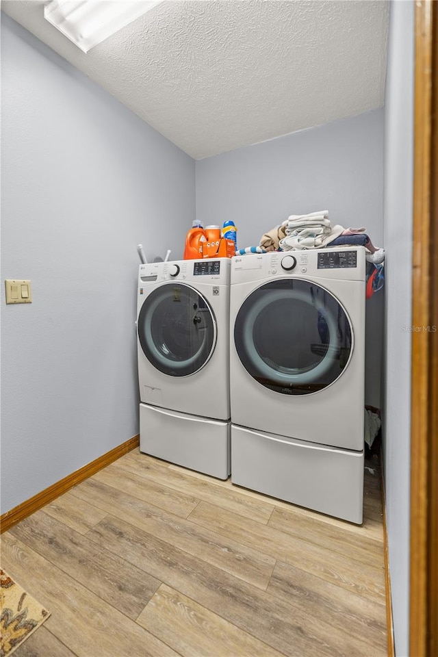 laundry area featuring washing machine and clothes dryer, a textured ceiling, and light hardwood / wood-style flooring