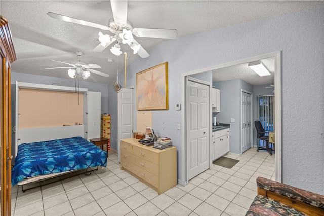 bedroom with a textured ceiling, connected bathroom, light tile patterned floors, and ceiling fan