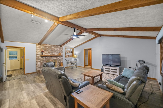 living room featuring a textured ceiling, light hardwood / wood-style flooring, a brick fireplace, ceiling fan, and lofted ceiling with beams