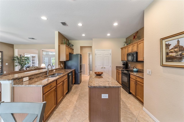 kitchen featuring black appliances, kitchen peninsula, sink, light stone countertops, and a kitchen island