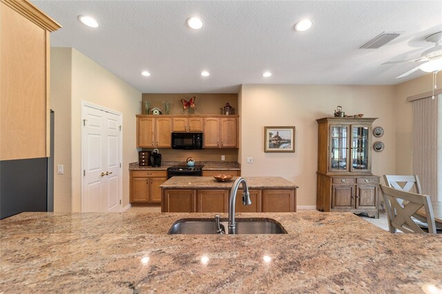 kitchen featuring a textured ceiling, light stone countertops, black appliances, sink, and ceiling fan