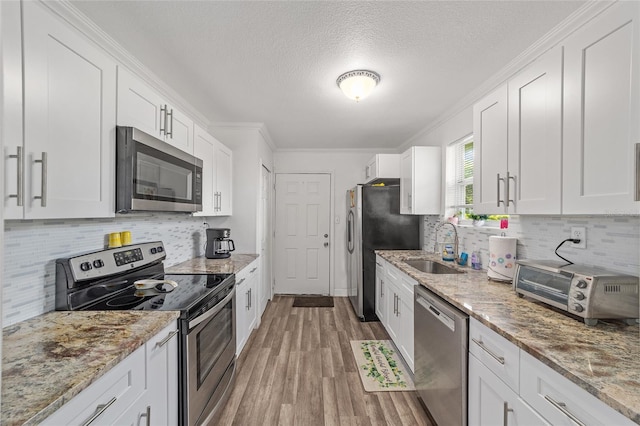 kitchen featuring stainless steel appliances, white cabinets, crown molding, and light stone countertops