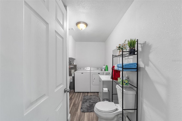 bathroom with washing machine and clothes dryer, a textured ceiling, hardwood / wood-style floors, toilet, and water heater