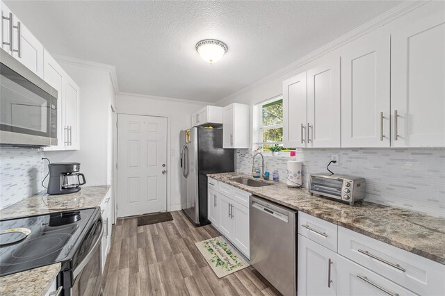 kitchen featuring light stone counters, stainless steel appliances, white cabinets, and sink