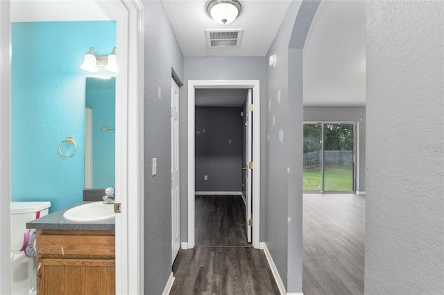 hallway featuring sink, dark wood-type flooring, and a textured ceiling