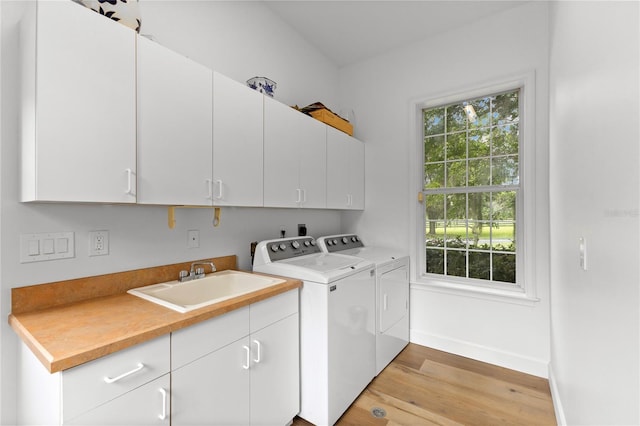 clothes washing area featuring light hardwood / wood-style flooring, sink, washer and clothes dryer, and cabinets