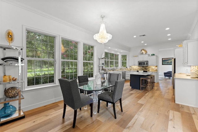 dining room with an inviting chandelier, crown molding, and light hardwood / wood-style flooring